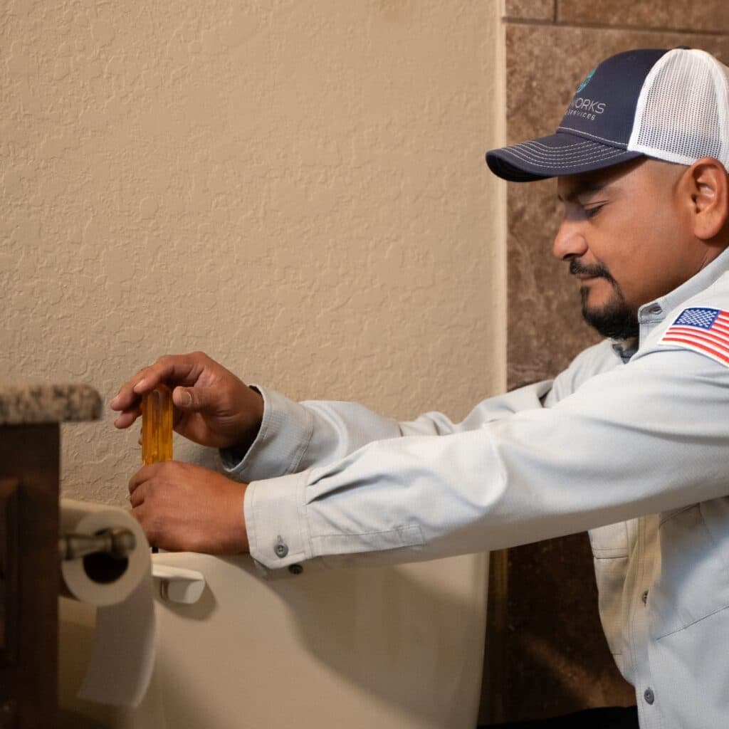 drainworks plumber using a screwdriver to fix a toilet in a san antonio home