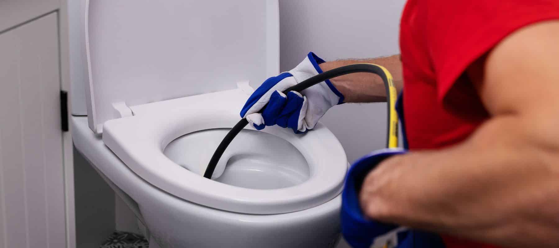 plumber wearing blue and white gloves using a hydrojetting tool to clear a toilet drain