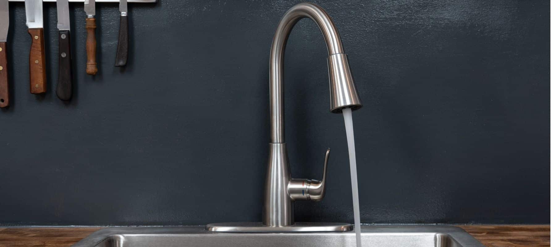 closeup of a kitchen sink with water running out of it and knives hanging on a magnetic strip
