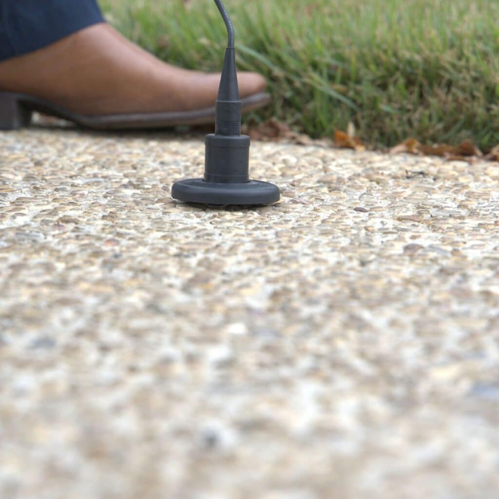 closeup of a gravel sidewalk with a leak detection tool looking for a leak under the sidewalk