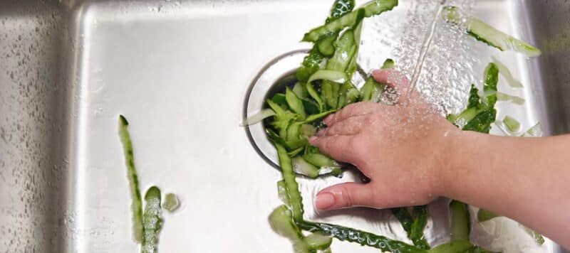large amounts of a green vegetable being pushed down a sink drain
