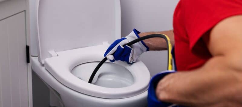 closeup of a plumber using a drain snake to hydrojet a residential toilet