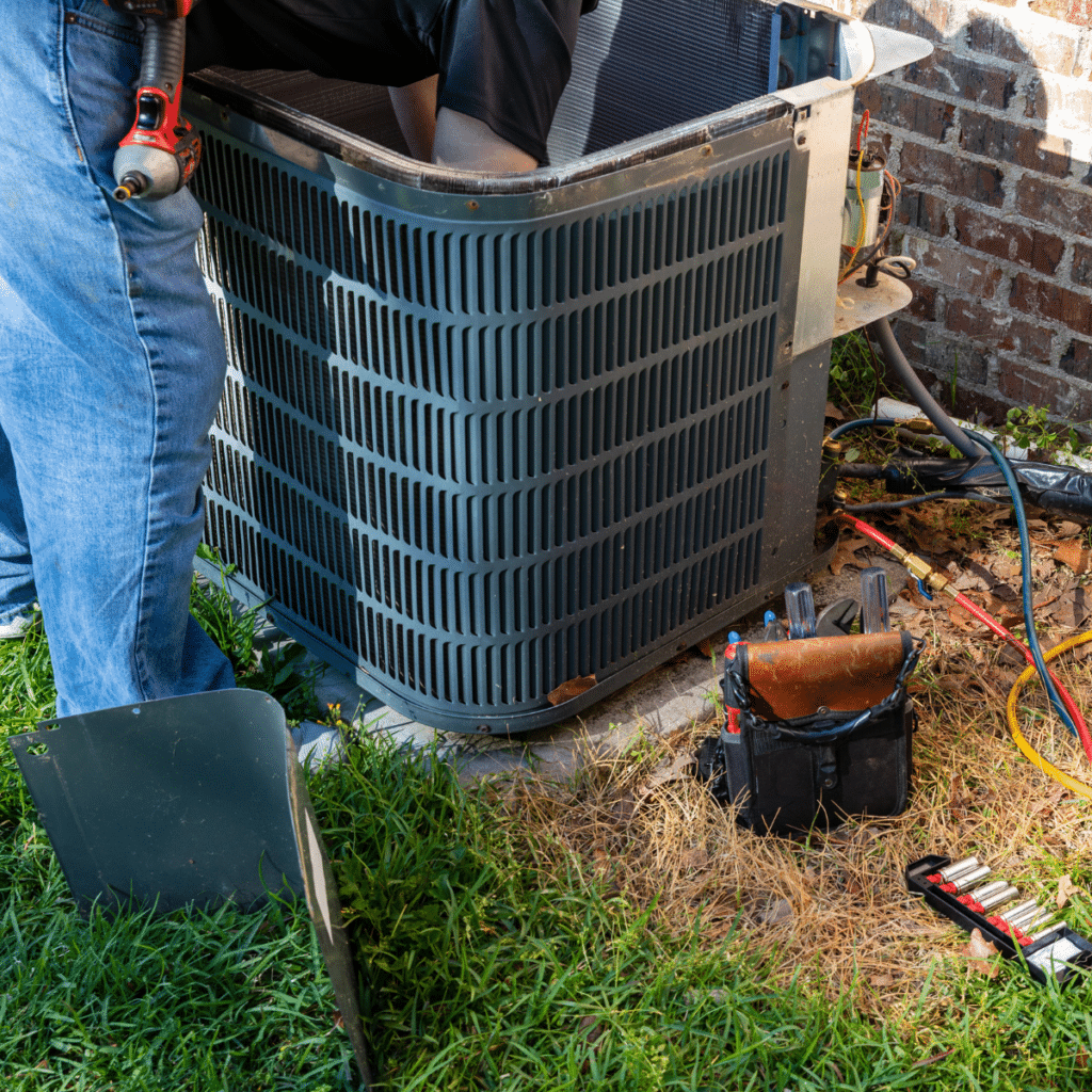 Outdoor HVAC unit under maintenance with visible tools, wiring, and gauges placed on the ground