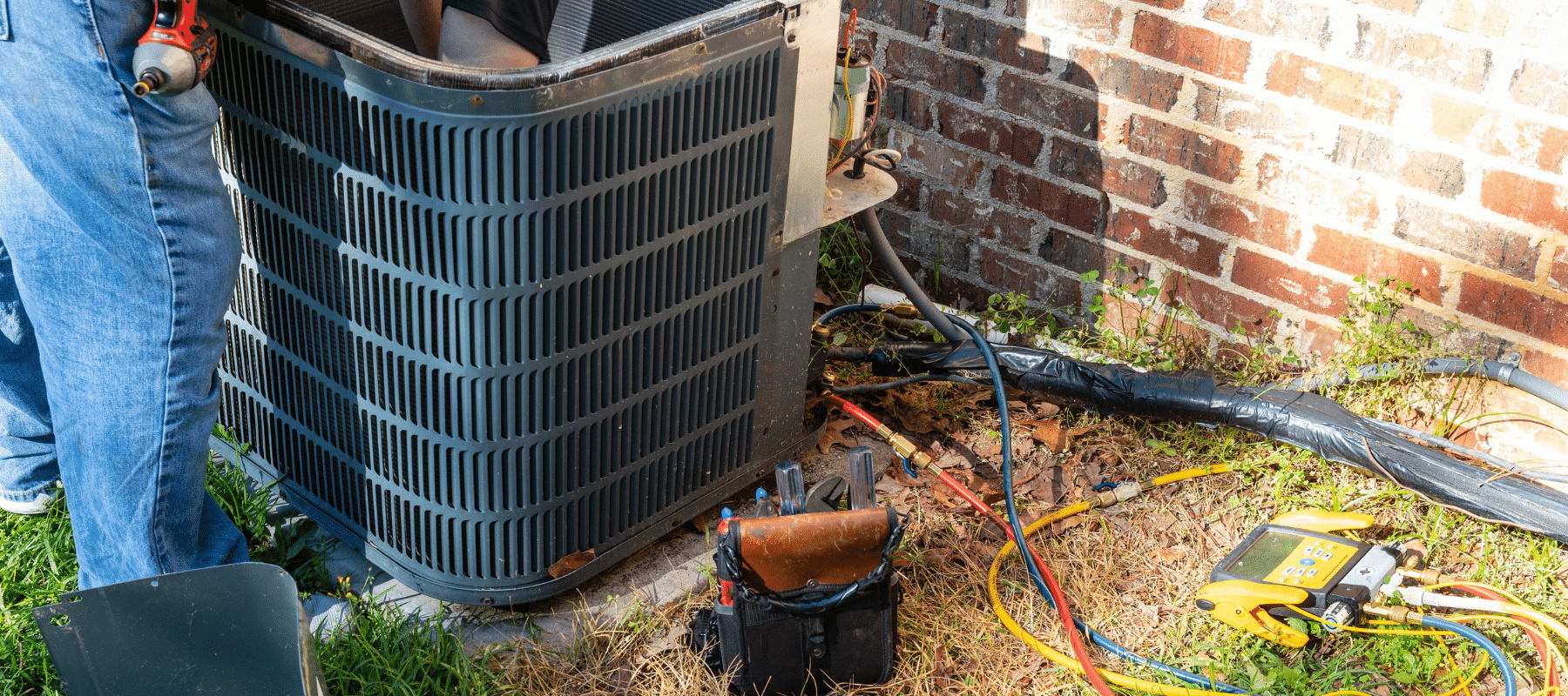 Outdoor HVAC unit under maintenance with visible tools, wiring, and gauges placed on the ground