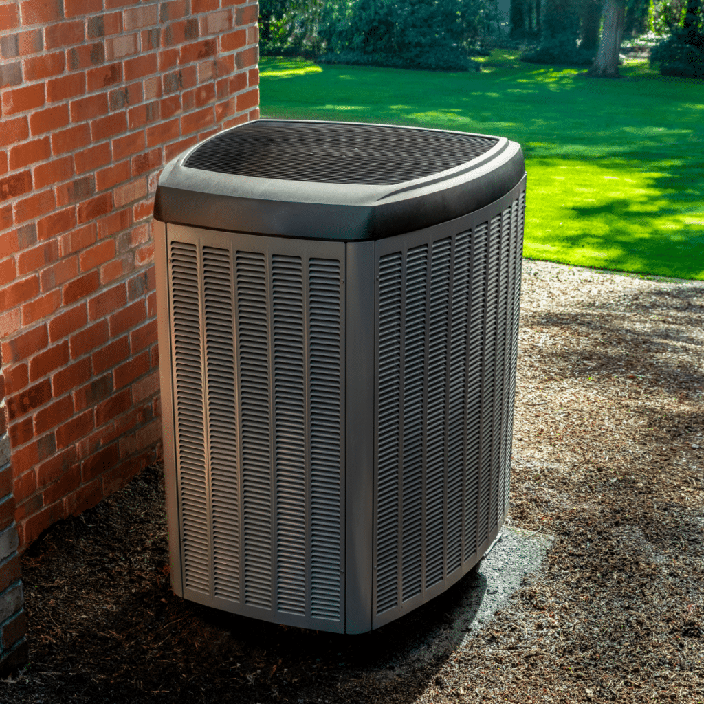 An isolated outdoor HVAC unit positioned near a red brick wall in a landscaped yard