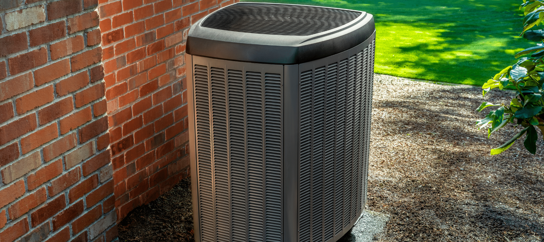 An isolated outdoor HVAC unit positioned near a red brick wall in a landscaped yard