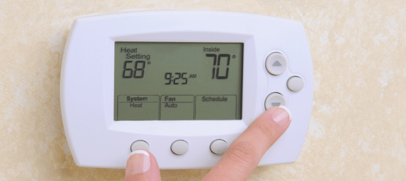 hand reaching up to a programmable thermostat to set the temperature