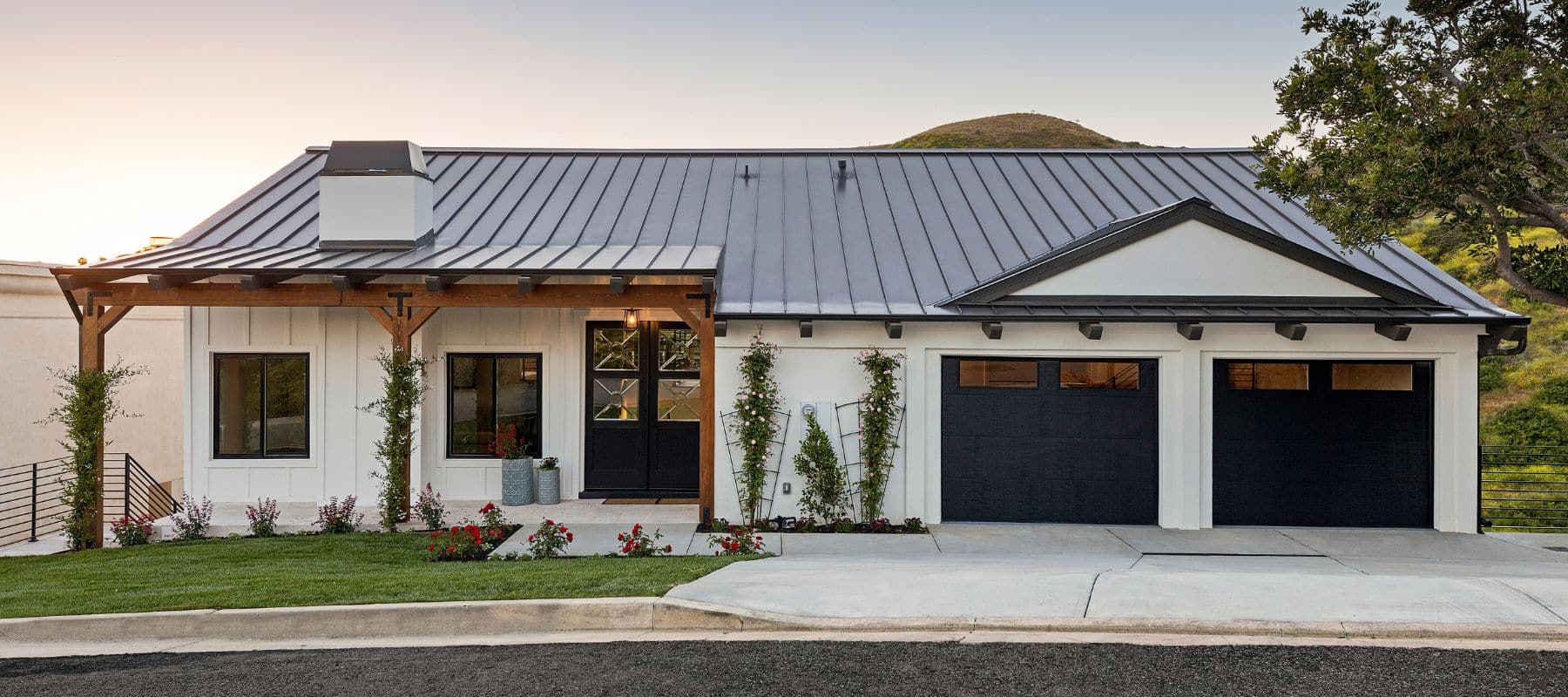 Modern farmhouse with black metal roof, white exterior, and dual garage doors in a suburban setting