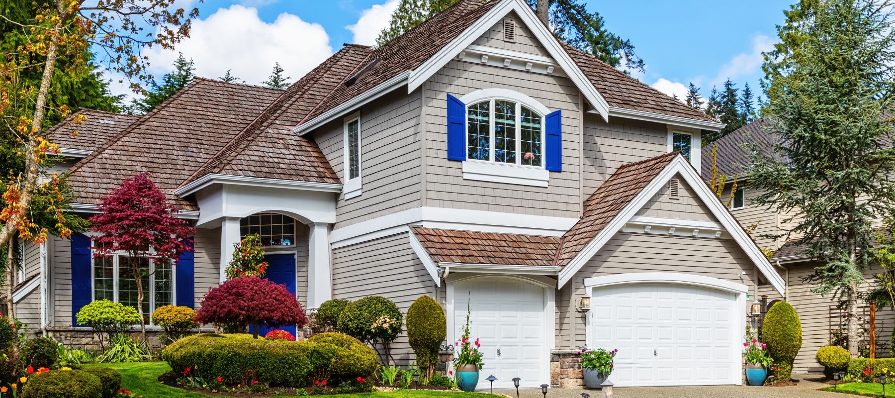 Elegant two-story home with shake siding, blue shutters, and manicured landscaping