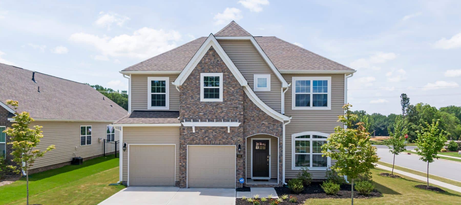 Two-story suburban home with stone facade, tan siding, and a double garage