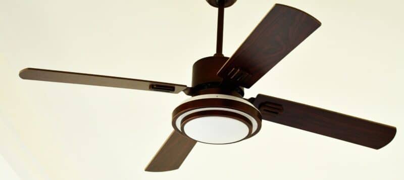 Close-up of a modern ceiling fan with wooden blades and a built-in light fixture, mounted on a white ceiling