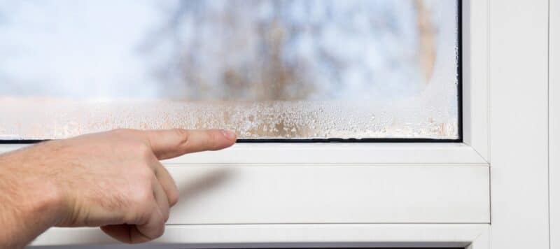 A hand pointing at condensation buildup between the panes of a double-glazed window