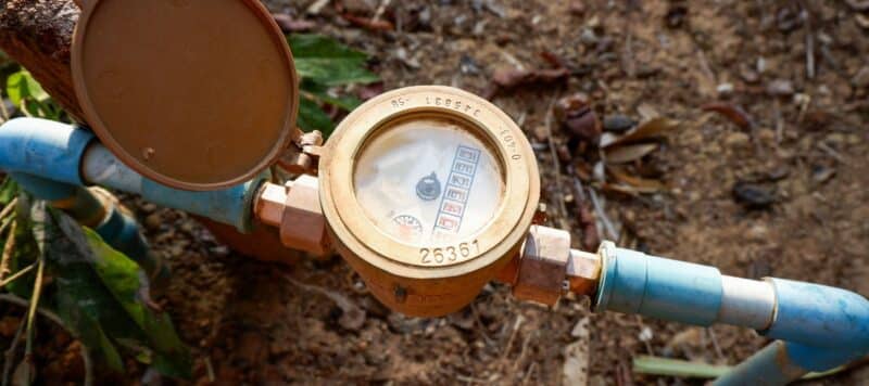 Outdoor water meter with blue pipes and an open cover showing the dial and reading numbers