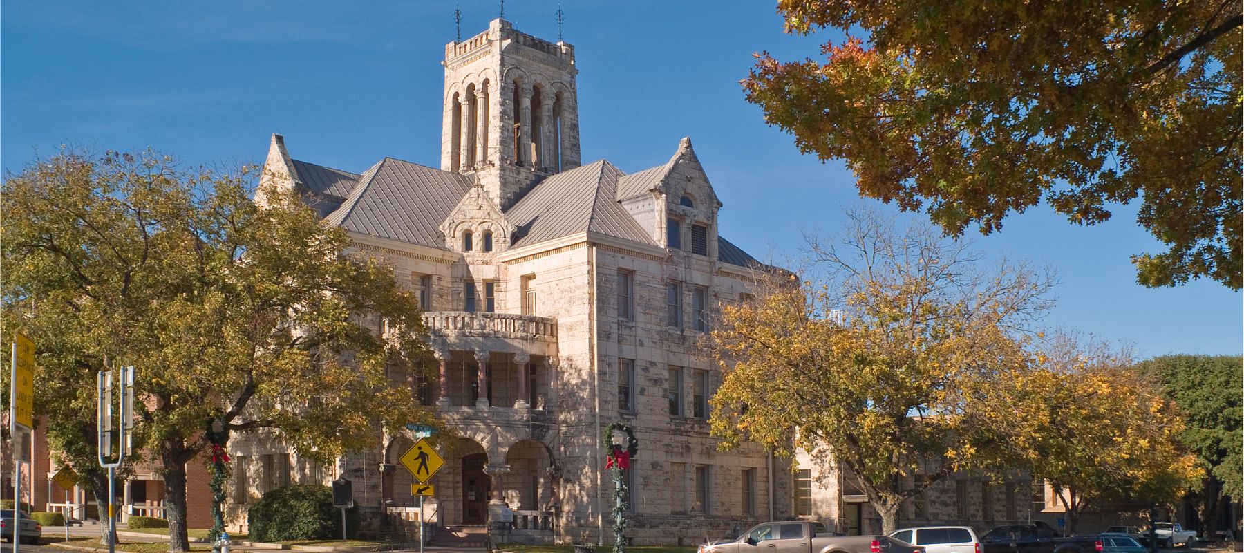 Historic stone courthouse in New Braunfels, Texas, framed by trees with autumn leaves