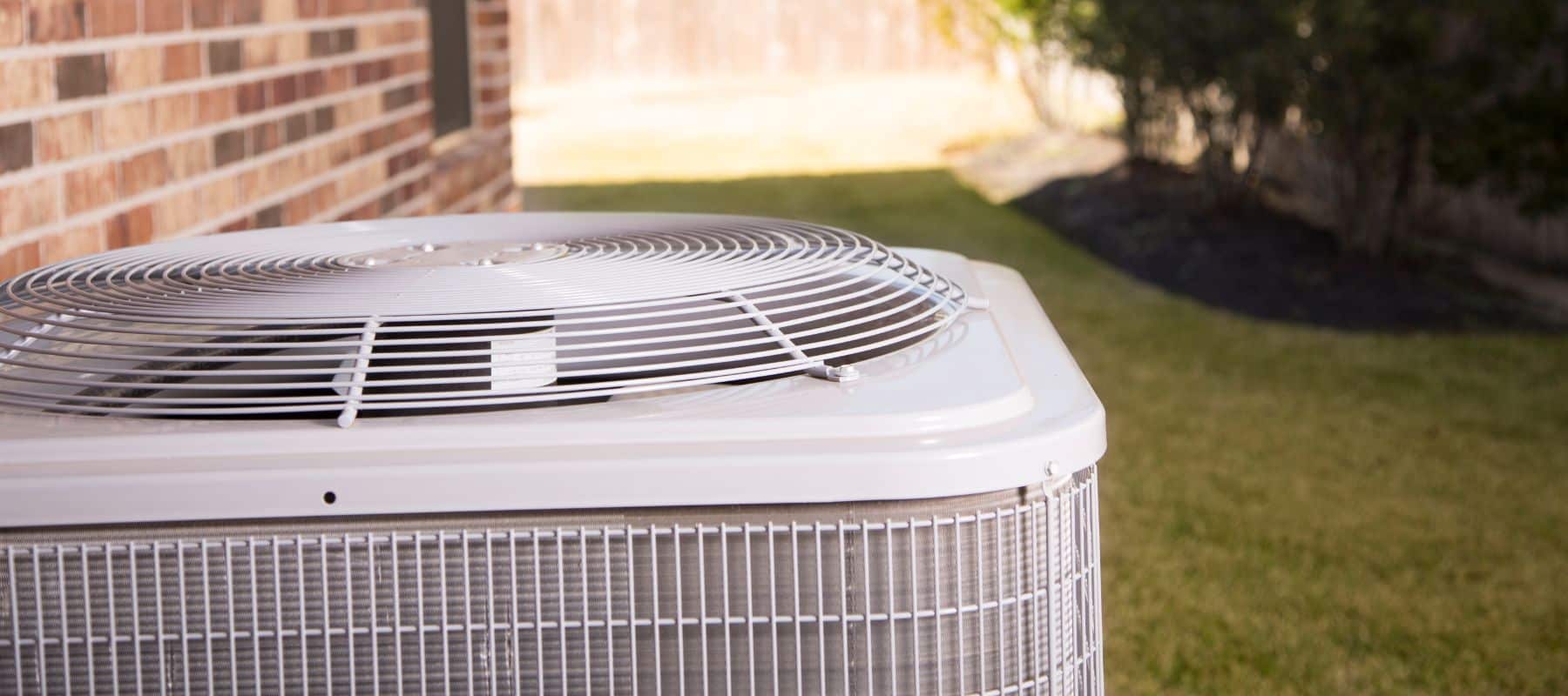 Close-up of an outdoor air conditioning unit next to a brick house on a sunny day