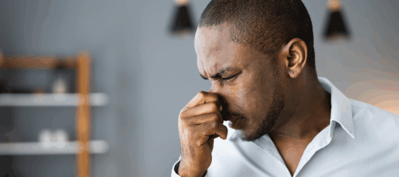 Man pinching his nose from a burning smell indoors, representing why a furnace may smell like burning in San Antonio, TX.