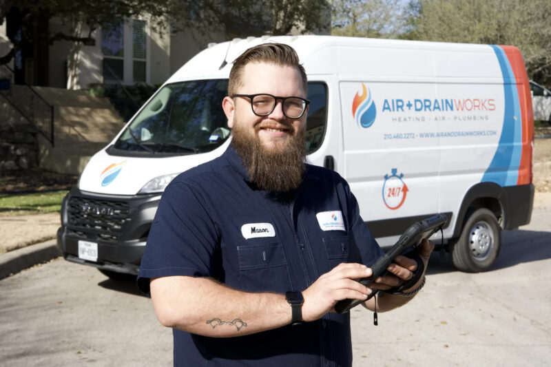 Male technician with a beard holds a tablet outside a service van.
